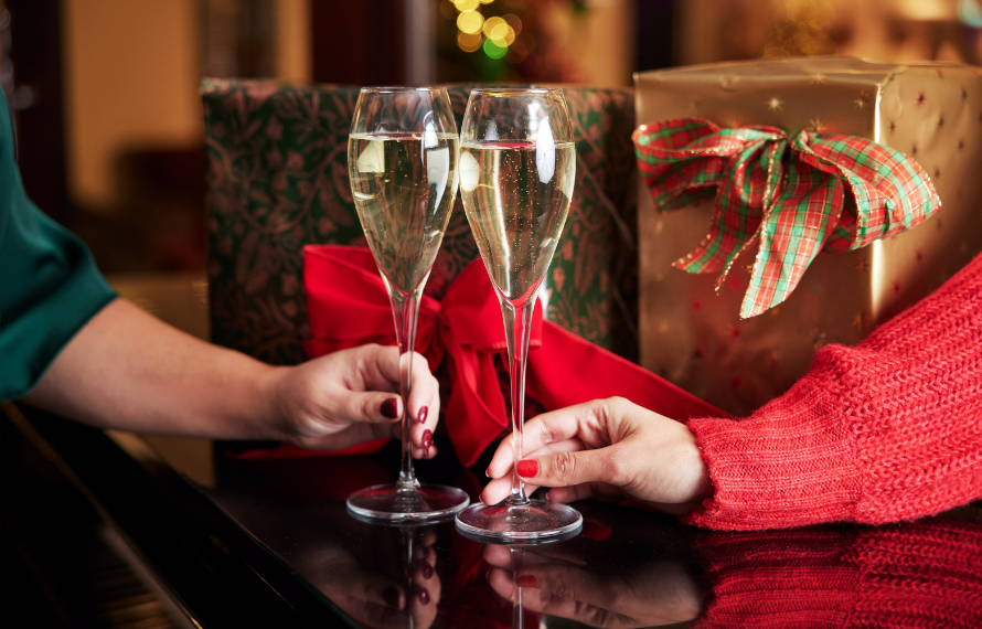 Two people toasting with champagne glasses in front of wrapped Christmas gifts