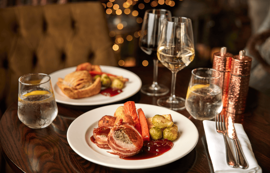 Festive table with Christmas dinner featuring roasted meats, vegetables, and wine glasses