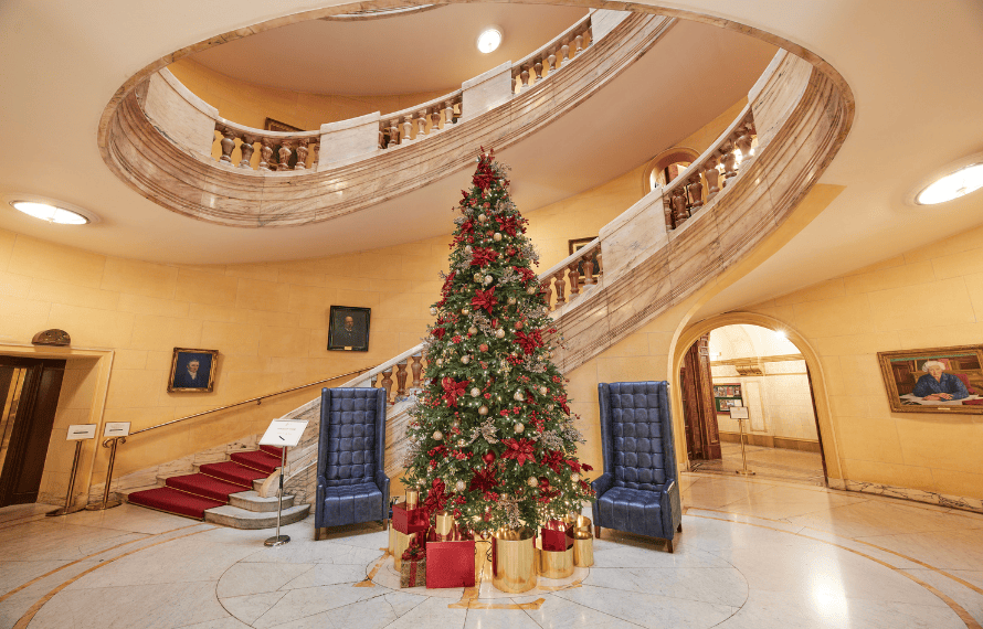 Ornate staircase with Christmas tree and red decorations in a grand hall